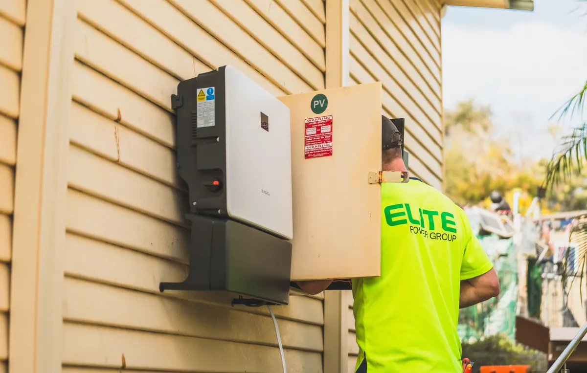 An electrician performs an outdoor equipment installation on the exterior wall of a home, the kind of site work involved in a generator installation
