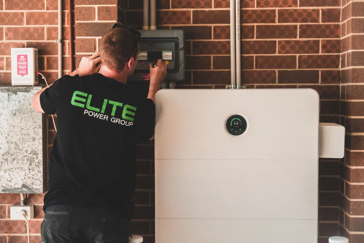 Electrician installing a home battery backup storage unit next to an electrical panel